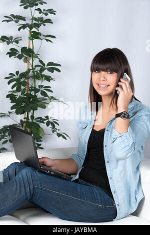 Junge, hübsche Frau sitzt auf dem Sofa und telefoniert Mit einem Smartphone. Foto Stock
