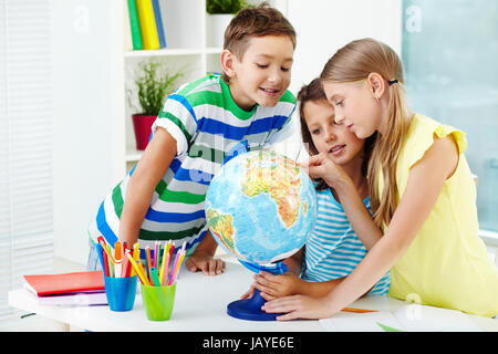 Ritratto di felice i compagni di scuola al lavoro studiando globe in aula Foto Stock