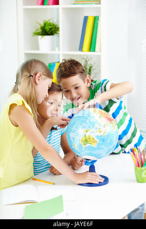 Ritratto di curiosi i compagni di scuola al lavoro studiando globe in aula Foto Stock