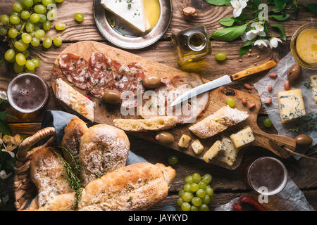 Il pane fatto in casa, formaggio, olive, uva e fiori su schede vecchia posizione orizzontale Foto Stock