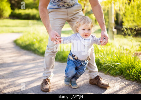 Irriconoscibile padre tenendo le mani di suo figlio prendendo i primi passi Foto Stock