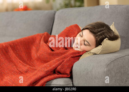 Ritratto di una ragazza dorme coperto con una coperta arancione giacente su un comodo divano nel salotto di casa Foto Stock