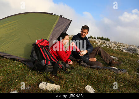 Junge Leute trinken beim Camping in den Bergen Alpen Foto Stock