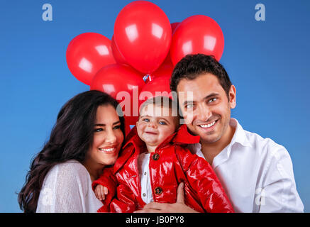 Closeup ritratto di giovani genitori portano il dolce adorabile figlio all'aperto, bellissimi palloncini rossi, uno stile di vita attivo, happy family concept Foto Stock