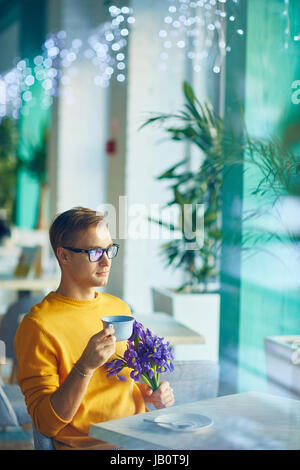 Uomo bello con bouquet di fiori in attesa in Cafe Foto Stock