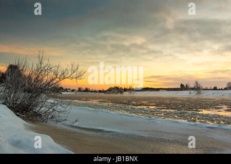 The sun sets over the freezing river causing the mist to rise from the cold water in the Northern Finland. Foto Stock