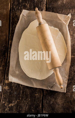 La preparazione di base per una pizza italiana con una vista aerea di pasta laminata su carta forno con un vecchio legno perno di rotolamento su di un legno rustico tavolo da cucina Foto Stock