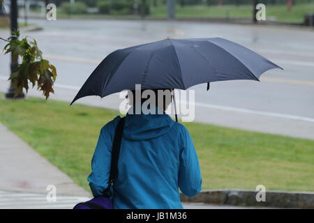 Donna che indossa un impermeabile blu che copre la sua testa con un ombrello Foto Stock
