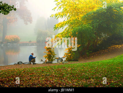 L'uomo la lettura di un libro di un lago in una nebbiosa mattina di autunno Foto Stock