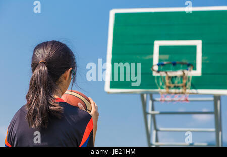 L'adolescente di sesso femminile sempre pronti a sparare un tiro libero basketball presso una piscina campo da pallacanestro su una luminosa giornata di sole Foto Stock