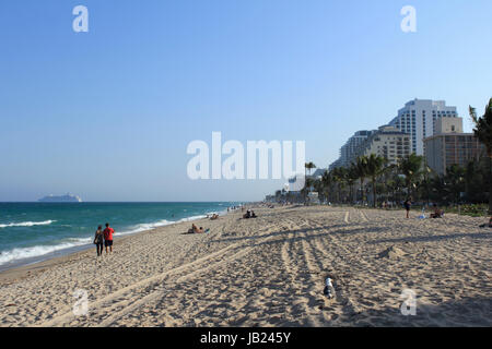 FORT LAUDERDALE, FLORIDA - MARZO 23, 2013: le persone che si godono una passeggiata serale lungo le rive di Fort Lauderdale Beach a destra prima del tramonto. Una nave da crociera è vista sull' Oceano Atlantico in background. Foto Stock