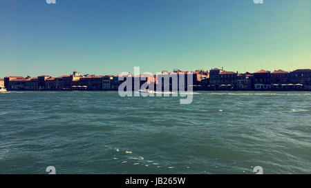 Immagine della fila di edifici sull'isola di contrasto contro le chiare acque blu del mare e del cielo a Venezia, Italia Foto Stock