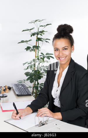 Junge Angestellte sitzt am Schreibtisch im Büro und schreibt in einen Aktenordner Foto Stock