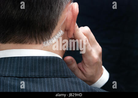 Close-up di un agente dei servizi segreti ascoltando il suo auricolare, dietro. Foto Stock