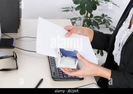 Junge Frau sitzt am Schreibtisch im Büro und locht Dokumente Foto Stock