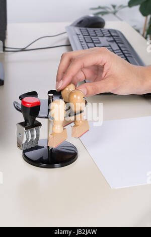 Junge Frau sitzt am Schreibtisch im Büro und greift nach einem Stempel Foto Stock