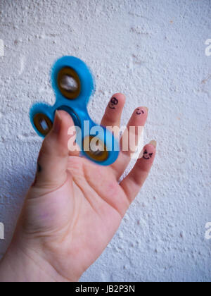 Una commovente agitano: spinner in una mano con differenti facce sorridenti sugli ultimi tre dita Foto Stock