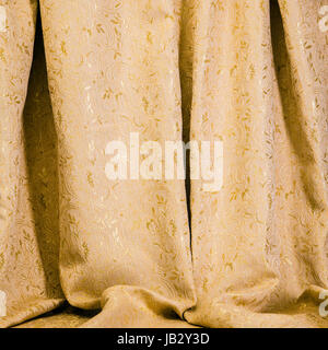 Texture di sfondo di drappeggi di golden damasco con un brillante self patterning di fiori e foglie di acanto appeso nella lussureggiante pieghe morbido per un elegante decor interno Foto Stock
