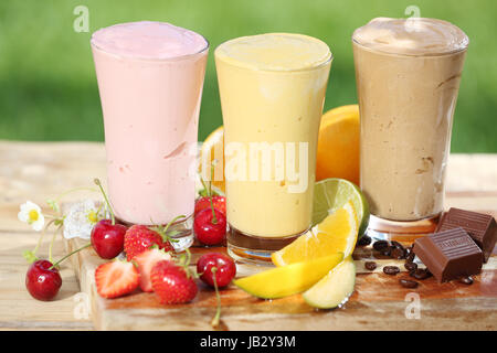 Tre deliziosi frullati con yogurt o gelato blend, due con frutta e uno di cioccolato con vari frutta fresca tropicale su un tavolo da giardino Foto Stock