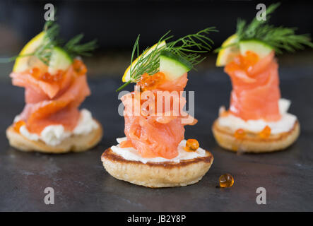 Blini con salmone affumicato e panna acida, guarnito con aneto. Vista da vicino su sfondo scuro Foto Stock