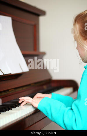 Bambino seduto ad un pianoforte a giocare indossando una treccia in i capelli biondi Foto Stock