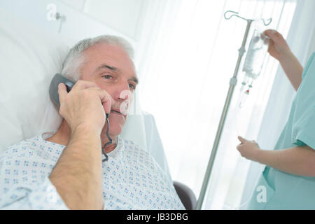 Vecchio paziente di sesso maschile utilizzando mobilephone al centro dialisi Foto Stock