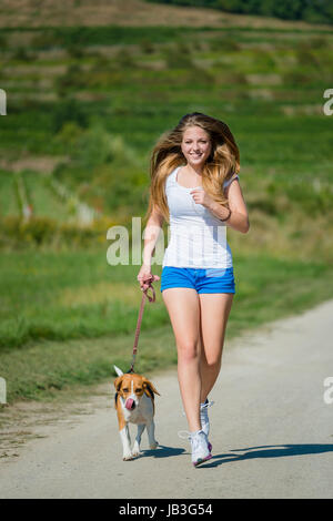 Bella ragazza adolescente jogging con il suo animale domestico (cane beagle) in natura Foto Stock