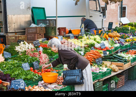 Locali francese donna guarda a verdura fresca impilati in modo attraente esposti per la vendita su uno stallo presso un mercato locale nella città vecchia a Annecy, Francia Foto Stock