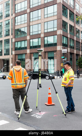 Due uomini in arancione e giallo giubbotti di sicurezza di funzionamento con il GPS su un treppiede in Manhattan inferiore Foto Stock