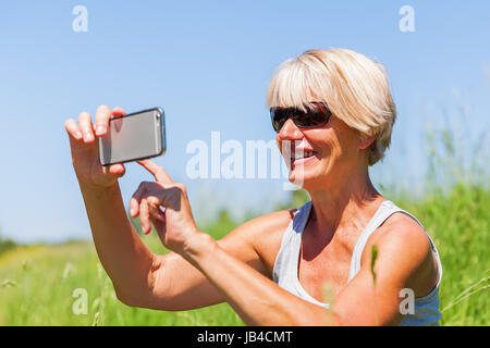 Vestito estivo donna matura selfie rende le foto con un telefono esterno Foto Stock