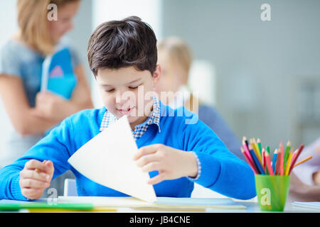 Ritratto di carino schoolboy seduto alla lezione sullo sfondo dei suoi compagni di classe Foto Stock