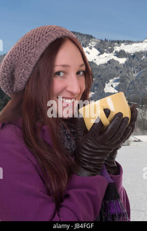 Junge Frau trinkt eine heiße Tasse Tee im Schnee in den Bergen im inverno Foto Stock