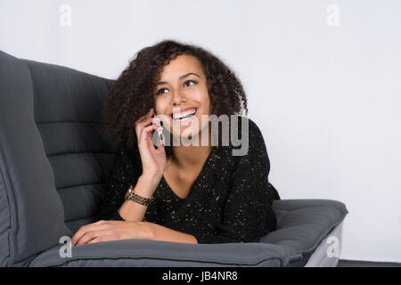Junge, hübsche Frau liegt auf dem Sofa und telefoniert Mit einem Smartphone Foto Stock