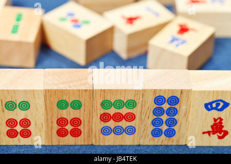 Piastrelle di legno closeup in mahjong gioco durante la riproduzione sul panno blu tabella Foto Stock