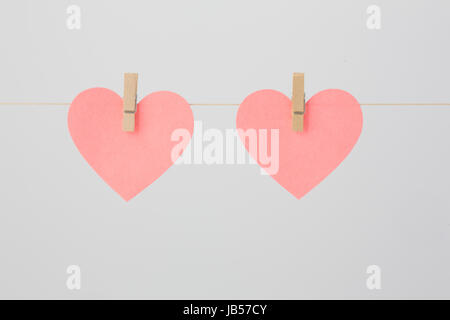 Due a forma di cuore rosa pezzi di carta attaccato ad un filo con clothespins in legno. Foto Stock