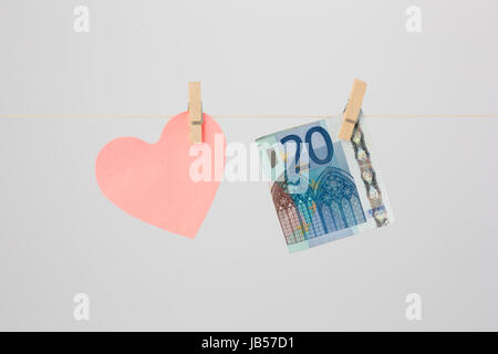 Un cuore rosa di carta a forma di nota e una ventina di Euro bill attaccato ad un filo con clothespins. Foto Stock