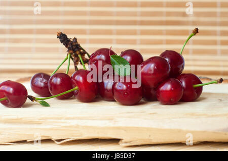 Close up fresco e appetitoso ciliegie su un pezzo di legno isolato su sfondo beige Foto Stock