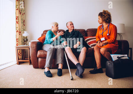 Coppia di anziani a parlare con loro healthcare lavoratore a casa. Essi sono sittig sul divano del soggiorno. Foto Stock