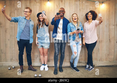 A sorridere e ridere di gruppo in bianco e nero di uomini e donne in piedi e tenendo selfie a parete in legno. Foto Stock