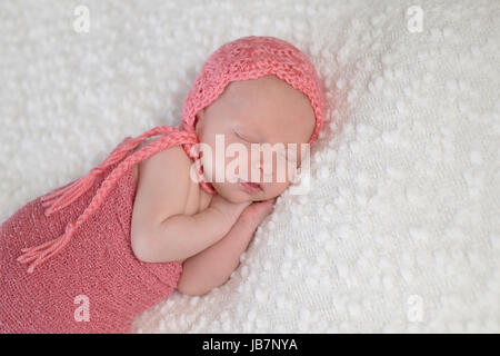 Ritratto di tre settimane vecchio sleeping neonato ragazza. Ella è swaddled e indossando una pesca colorata, maglia e del cofano è sdraiato su un bianco, bouncle Foto Stock