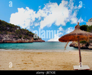 Kleiner Sandstrand in einer Bucht auf Mallorca, Steilküste mit Pinien; Sonnenschutz am Strand, blauer Himmel mit weißen Wolken piccola spiaggia di sabbia in una baia sul Maiorca, ripida costa con pini; protezione del sole in spiaggia, cielo blu con nuvole bianche Foto Stock