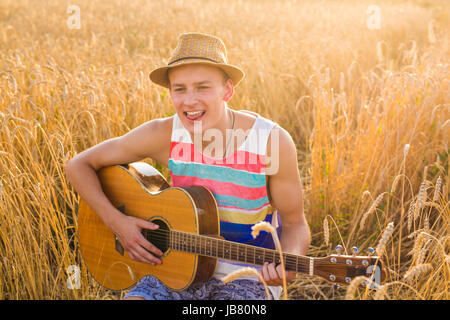 Un uomo sta suonando la chitarra nel campo di erba al giorno di relax con la luce solare Foto Stock