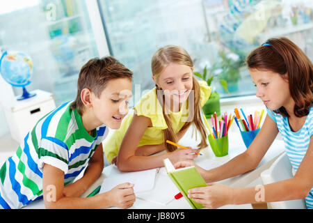Compagni di classe essendo curiosi di sapere che cosa i loro simpatico amico lettura Foto Stock