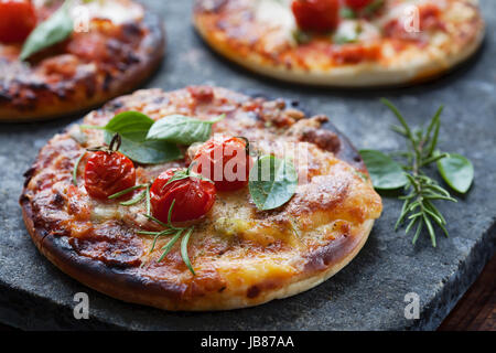 Pizzette con prosciutto, pancetta, formaggi e tomatoess Foto Stock