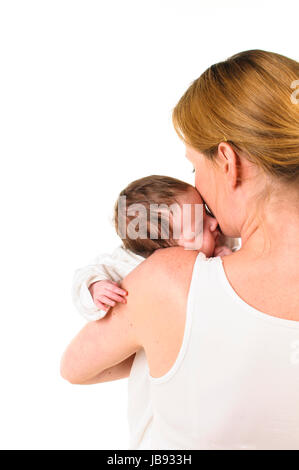 Eine erwachsene Frau mit weißem Shirt hält einen ebenfalls weiß gekleideten Säugling zärtlich auf dem braccio, freigestellt vor weißem Hintergrund. Foto Stock