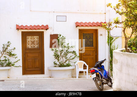 Rethymno, Grecia - 3 Maggio 2016: blu sport motocross moto parcheggiata di fronte bianco muro di pietra con porte di legno intagliato. Resort classic architetto greco Foto Stock