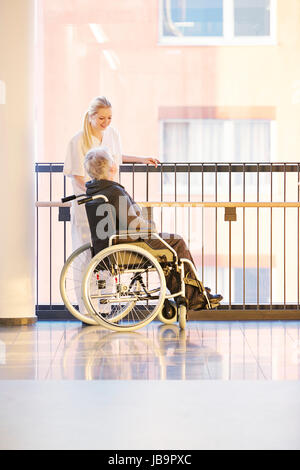 Rollstuhl und Patientin im Krankenhaus mit Krankenschwester im Gespräch Foto Stock