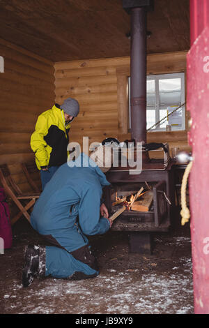 L'uomo mettendo log in stufa a legna a log cabin Foto Stock