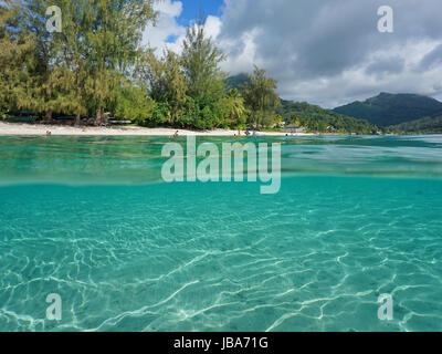 Al di sopra e al di sotto della superficie del mare vicino spiaggia tropicale a riva con un fondale sabbioso subacquea, Tariffa, Huahine isola, oceano pacifico, Polinesia Francese Foto Stock