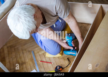 Uomo maturo con cacciavite elettrico durante la messa a scaffale o scaffale, vista da sopra Foto Stock